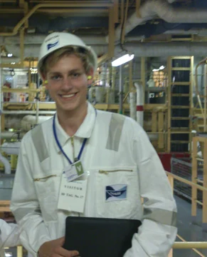 Jan in a factory, wearing a hard hat and protective coat