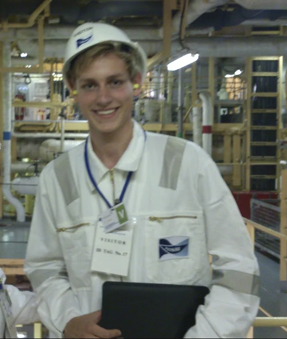 Jan visiting a factory, wearing a hard hat and protective coat
