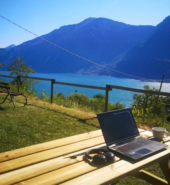 A laptop on an outdoor table overlooking a lake and mountains