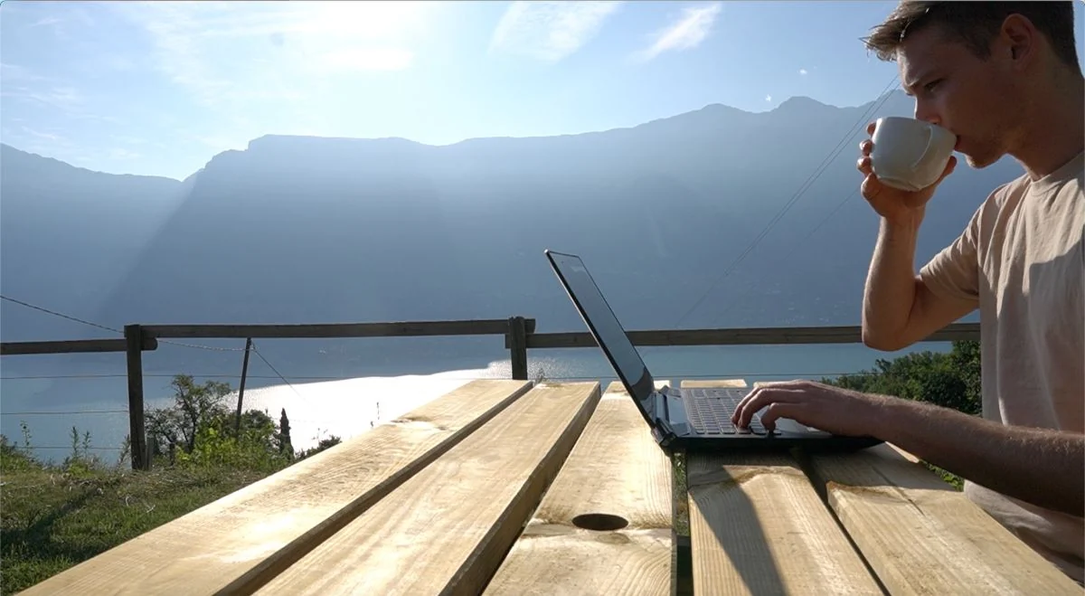 Jan working on his laptop outdoors with a view of mountains and a lake